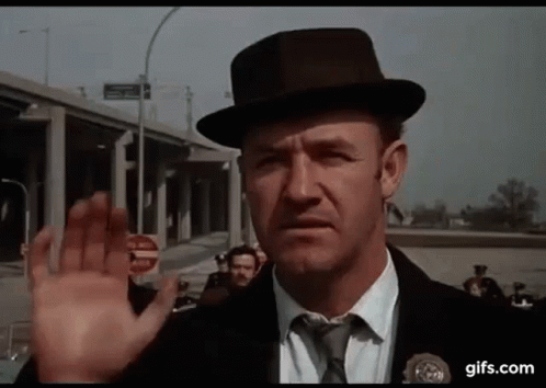 Gene Hackman wearing a black hat and waving goodbye