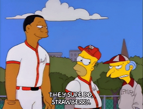 A Black baseball player folding his arms while talking to a couple of yellow-skinned baseball players.