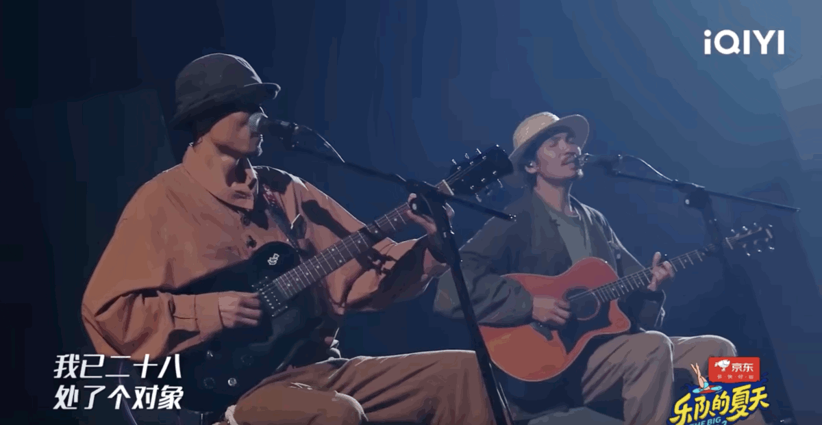 A screenshot from YouTube of two men playing the guitar. They are seated and singing into microphones. One is playing an electric guitar is wearing a black bowler hat, the other is playing a brown acoustic guitar and is wearing a white Panama hat. It has a very chill vibe