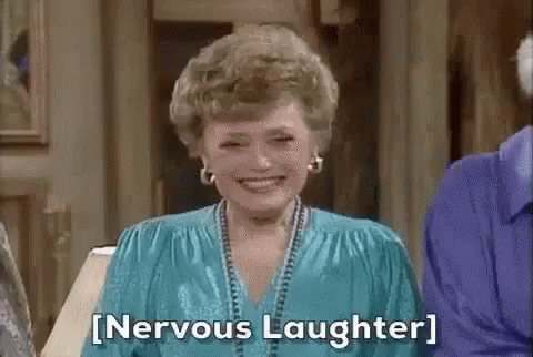 A white woman with blonde hair and an aqua-colored blouse laughing nervously.