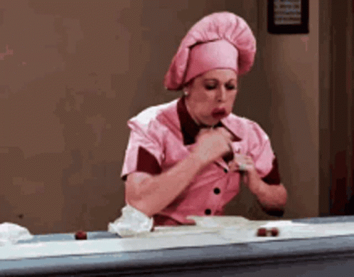 a woman in a pink apron picking up chocolates off a conveyor belt