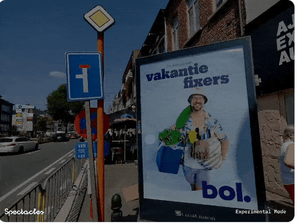 A short animated GIF shows a city street scene where an ad-blocking visual effect occurs in real life. The animation begins with the viewer looking at a large, colorful billboard advertisement for the company bol.com; the ad shows a smiling tourist in beach attire. Suddenly, a red screen resembling a digital "ad blocker" appears on top of the ad. Text in the corner reads “Spectacles Experimental Mode”. The video moves around in a slightly jagged way, indicating you're looking through the eyes of a person wearing the goggles