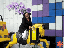 a woman riding a fake yellow horse while wearing a large flowered hat