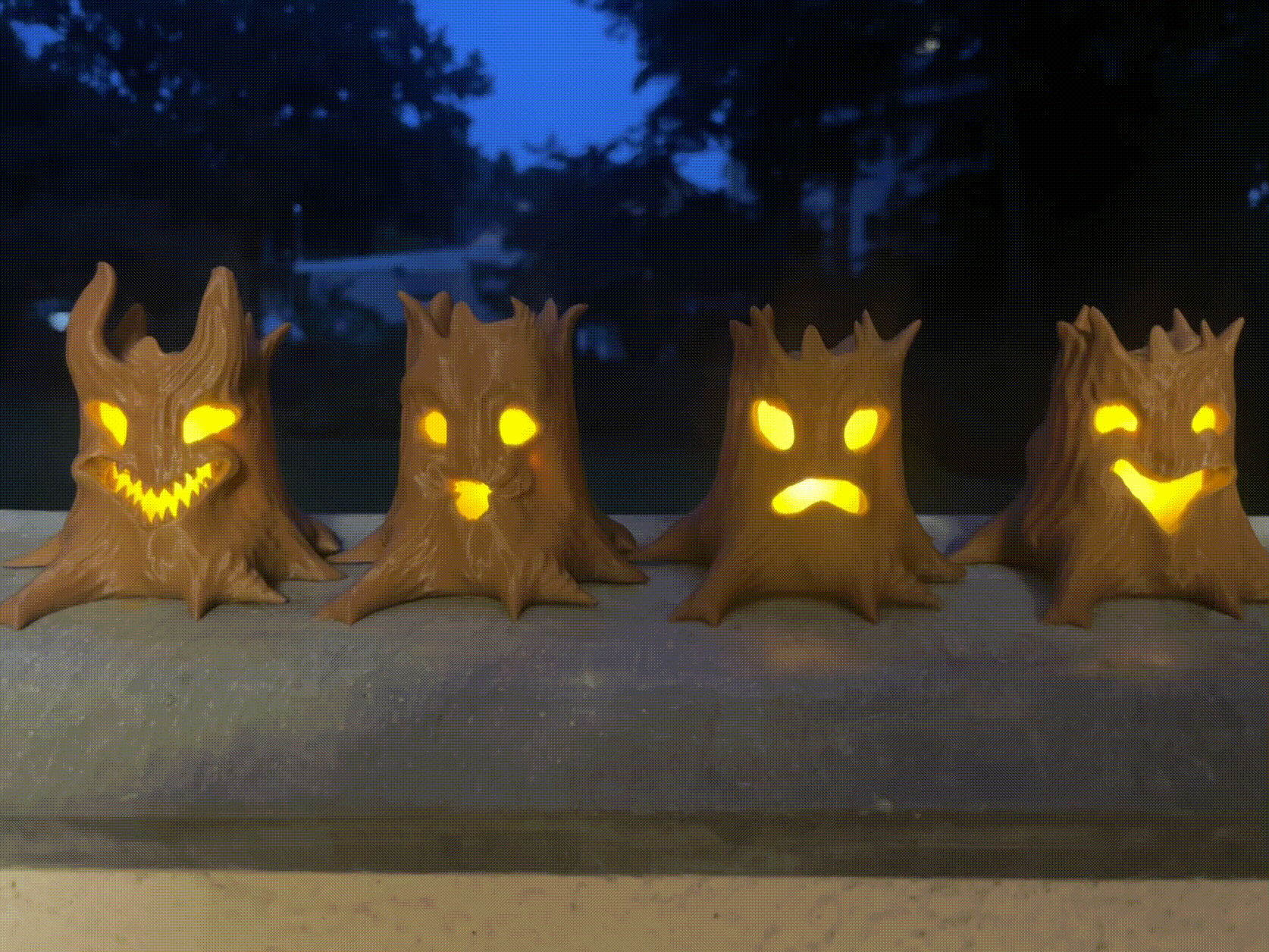 A grouping of tree stumps with different styled faces, illuminated from within by a flickering tea light