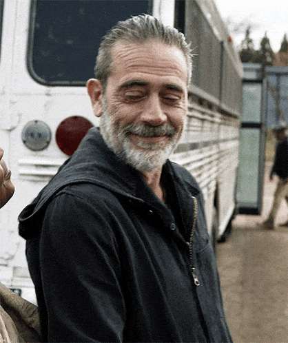 A bearded man standing next to a bus and laughing