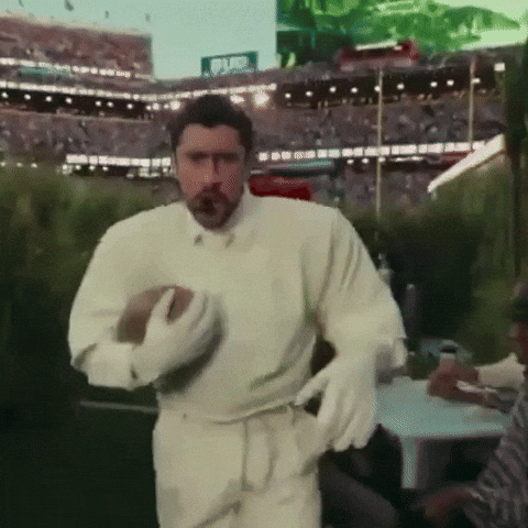 Gif mostra Bad Bunny em sua lendária apresentação no Super Bowl dando um tchauzinho com uma mão e segurando um ovo de "futebol americano" na outra