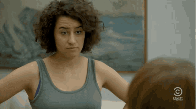 woman with dark curly hair in a green tank top replying with air quotes "How 'am' I?"