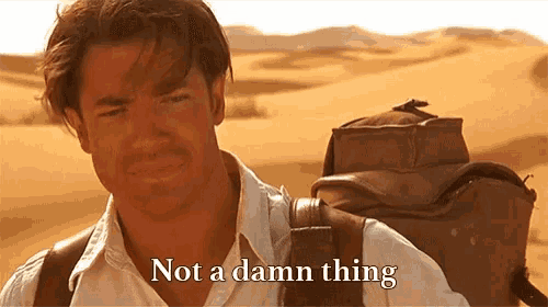 A man in a white shirt, with desert in the background, shaking his head saying, "Not a damn thing."