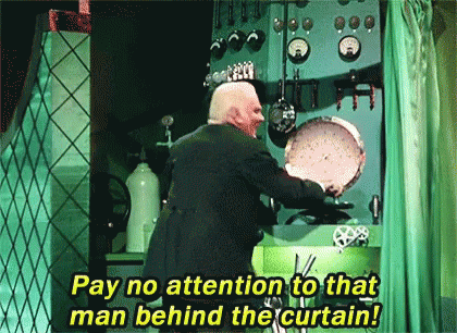 An older white man in a dark suit pulls a green curtain closed and says, "Pay no attention to that man behind the curtain."