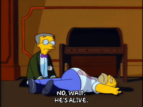 Homer Simpson wiggling on the ground while another man says, "No wait. He's alive."