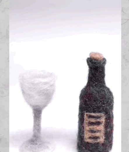 A looping gif showing a short bit of stop-motion animation. In the animation, a human hand opens a minature bottle of wine, made of felt, using a corkscrew, also made of felt. The hand then lifts the bottle and pours some felt red wine into a felt glass.