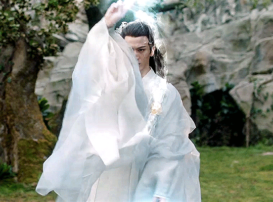 Changheng, god of war, from the C-Drama Love Between Fairy and Devil, a young immortal man in white and blue robes moving his arms wide and around to create defensive magic