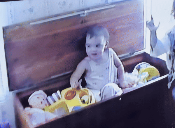 Home footage of a young Amelia signing into the camera, the thumb, index finger and pinky of one of her hands extended.