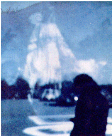 What looks like an out-of-focus, double-exposure, with the blurry shape of a figure in the foreground and the ghostly shape of Mary floating in the sky in the background.