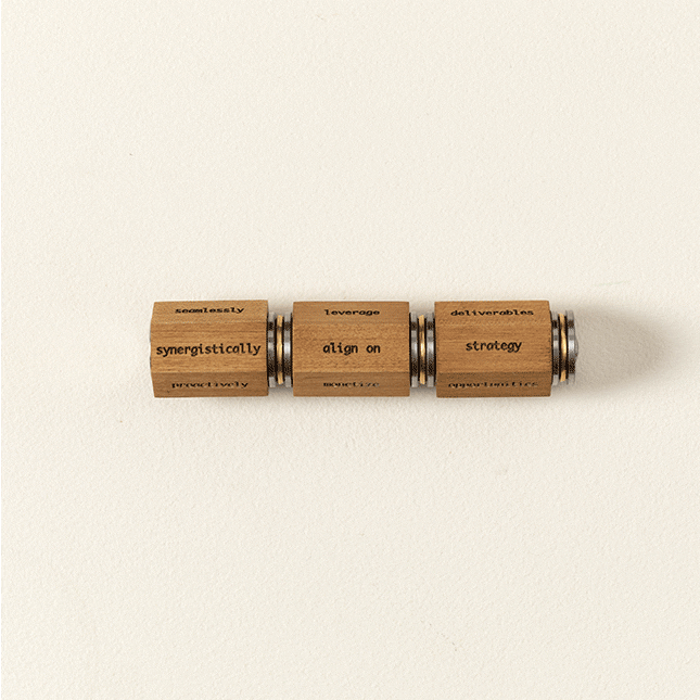An animated gif showing three hexagonal wooden cylindrical pieces. Each piece has corporate buzzwords written on each surface — like "stakeholders", "monetize", "opportunities", and "deliverable". In the animated gif, the pieces are spun around and recombined in different ways so that they spell nonsense corporate phrases like "actualize stakeholders proactively". The overall effect is funny and silly