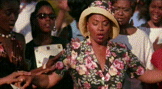 A black woman in a floral dress and hat faints backwards into a crowd.