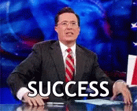A seated white man in a black suit and red tie pumping his fist above the word success.