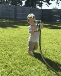 a toddler playing with a hose and spraying themselves in the face