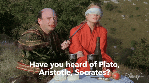 A white, bald man holding a knife to the throat of a blindfolded woman in a red dress and saying, "Have you heard of Plato, Aristotle, Socrates? Morons."