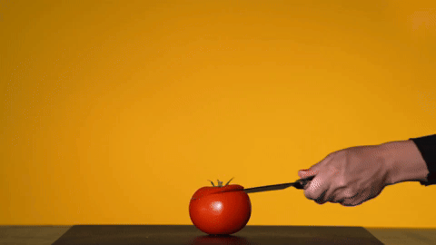 a person cutting a tomato which then squirts blood